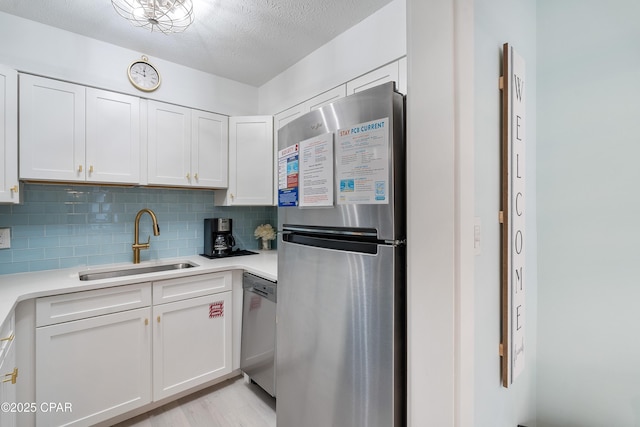 kitchen featuring a sink, backsplash, white cabinetry, light countertops, and appliances with stainless steel finishes