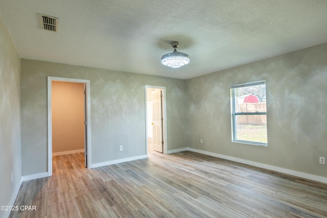 unfurnished room with visible vents, baseboards, a textured ceiling, and wood finished floors