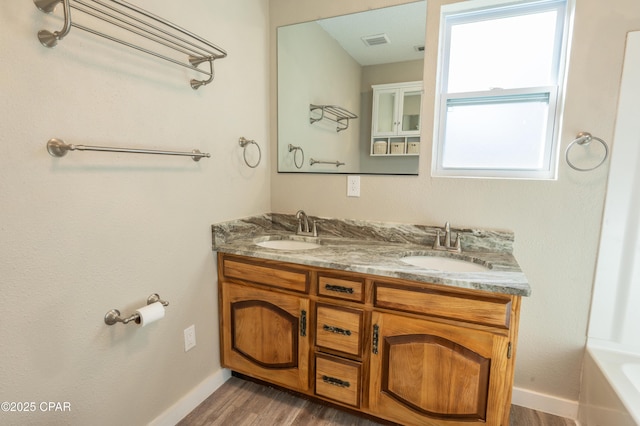 full bath with double vanity, wood finished floors, visible vents, and a sink