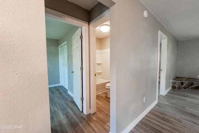 hall featuring a textured wall, baseboards, and dark wood-style flooring