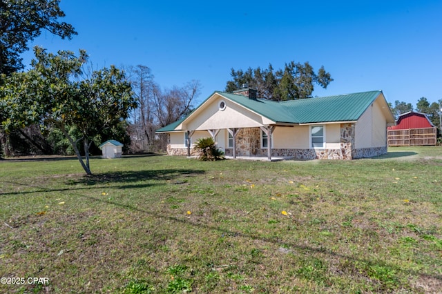 ranch-style house featuring a front yard, stucco siding, an outdoor structure, stone siding, and a storage unit