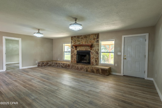 unfurnished living room featuring a stone fireplace, wood finished floors, baseboards, and a textured ceiling