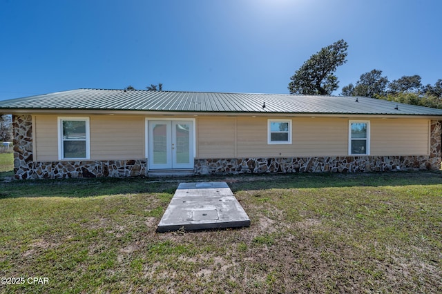 view of front of home featuring stone siding, french doors, metal roof, and a front lawn