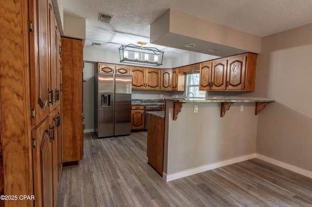 kitchen featuring brown cabinets, stainless steel fridge, a peninsula, a breakfast bar area, and dark wood-style flooring