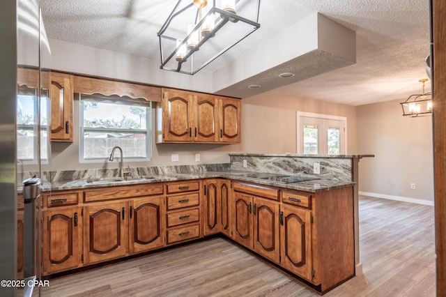 kitchen featuring a peninsula, black electric cooktop, brown cabinetry, and a sink