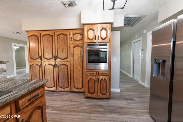 kitchen with visible vents, brown cabinets, dark wood-type flooring, and appliances with stainless steel finishes