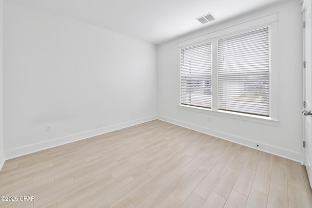 empty room featuring light wood-style floors, visible vents, and baseboards