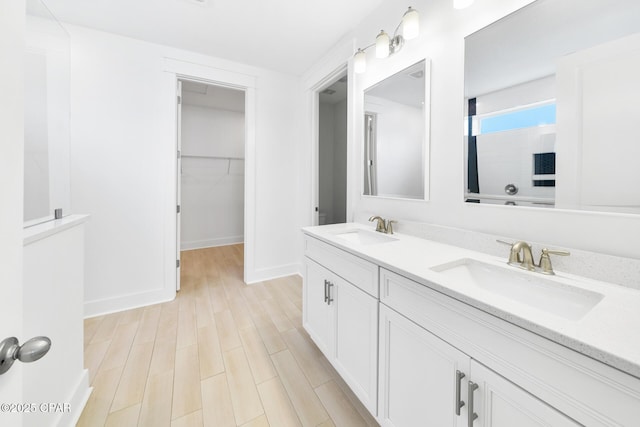 bathroom with wood finished floors, a walk in closet, walk in shower, and a sink