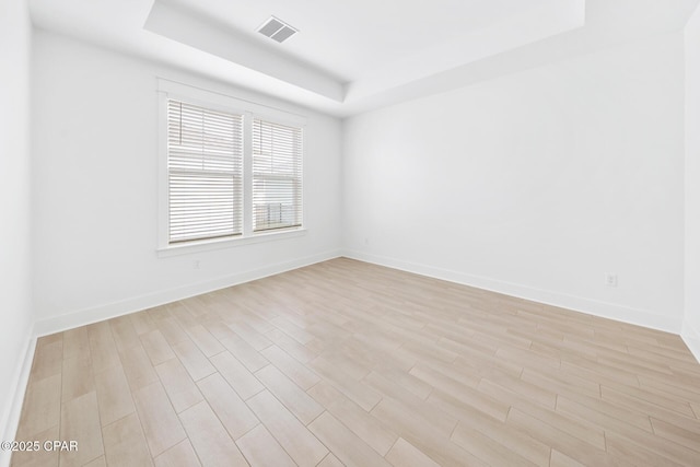 empty room featuring light wood finished floors, visible vents, baseboards, and a tray ceiling