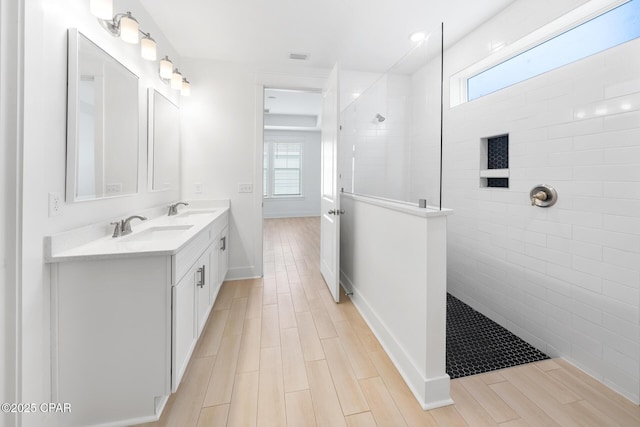 bathroom featuring wood tiled floor, a walk in shower, double vanity, and a sink