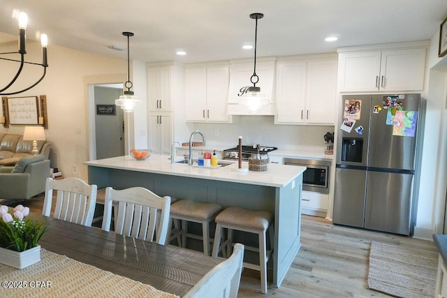 kitchen featuring a breakfast bar, light wood-style flooring, a sink, stainless steel appliances, and white cabinets