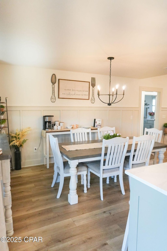 dining space with a notable chandelier, light wood-style flooring, a decorative wall, and a wainscoted wall