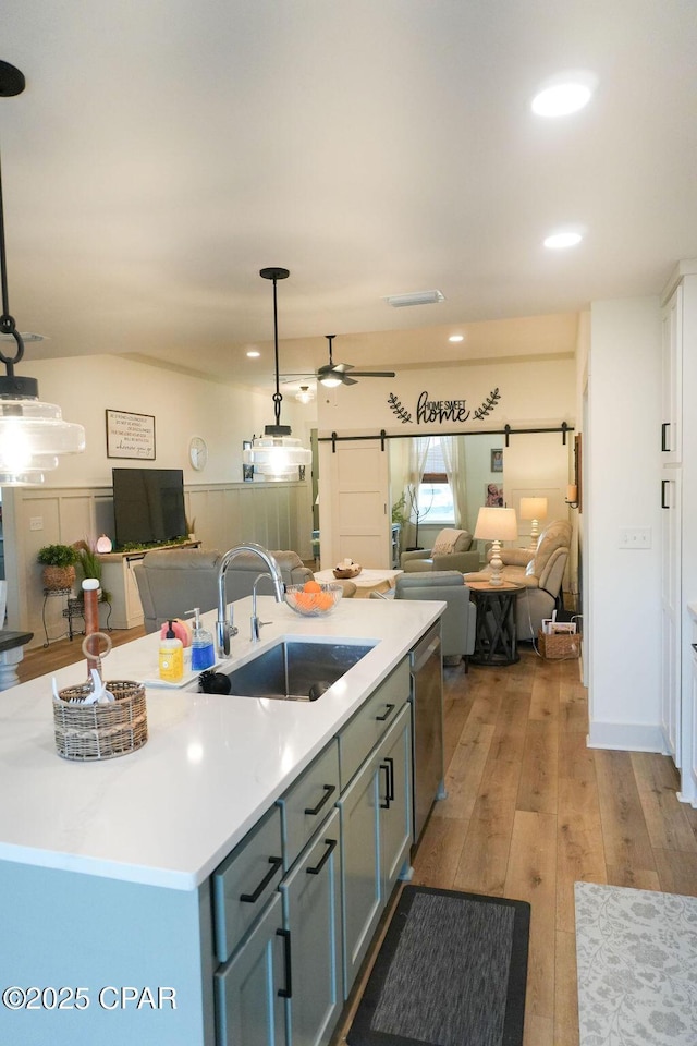 kitchen with open floor plan, dishwasher, a barn door, light wood-style floors, and a sink