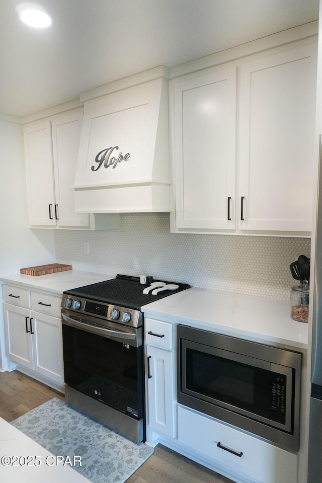 kitchen with appliances with stainless steel finishes, white cabinetry, light countertops, and custom range hood