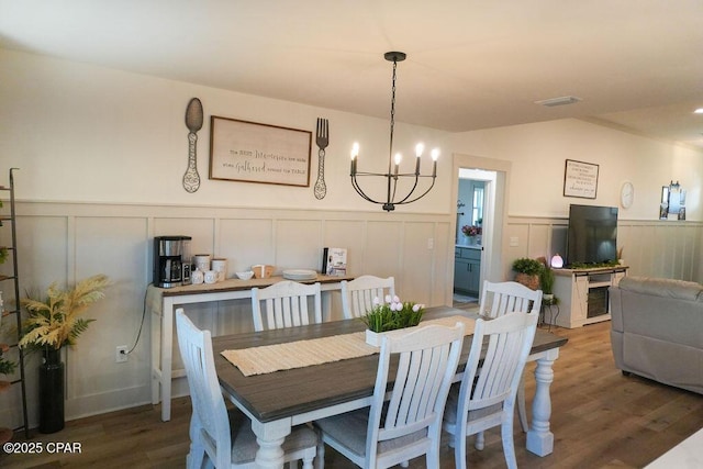 dining space featuring visible vents, a wainscoted wall, vaulted ceiling, wood finished floors, and a notable chandelier