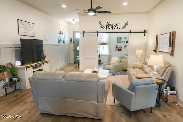 living room with a ceiling fan, wood finished floors, recessed lighting, wainscoting, and a barn door