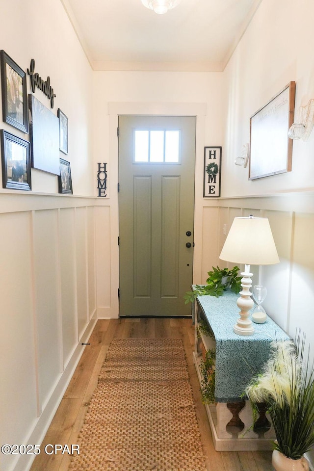 doorway with a decorative wall, wainscoting, and wood finished floors