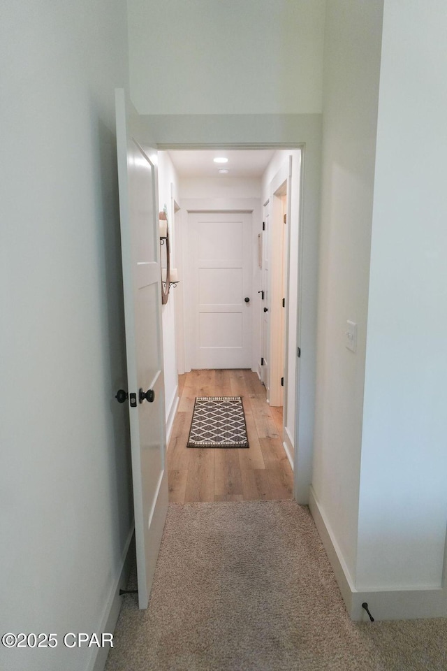 hall featuring baseboards, light carpet, and light wood-style flooring