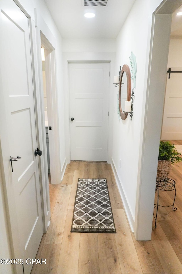 corridor with light wood finished floors, visible vents, and baseboards