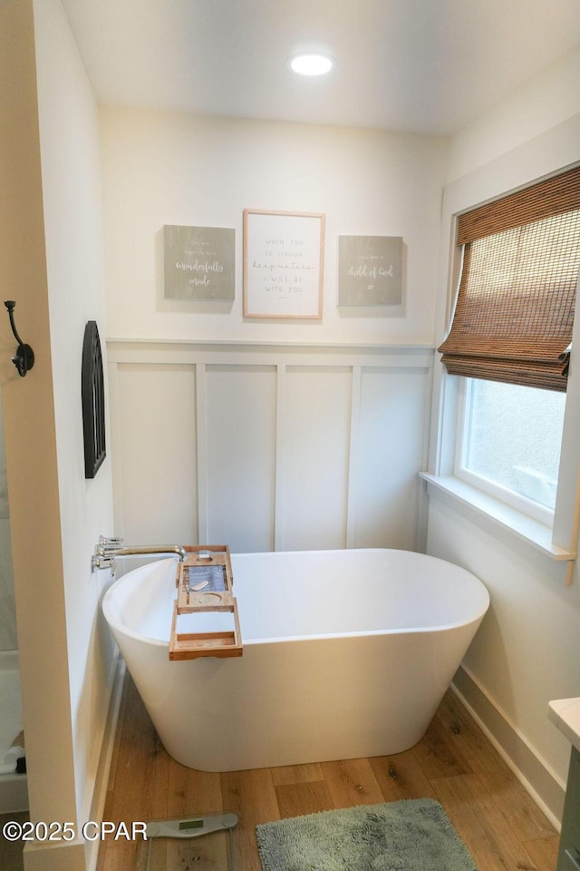 full bathroom with a decorative wall, wood finished floors, and a freestanding bath