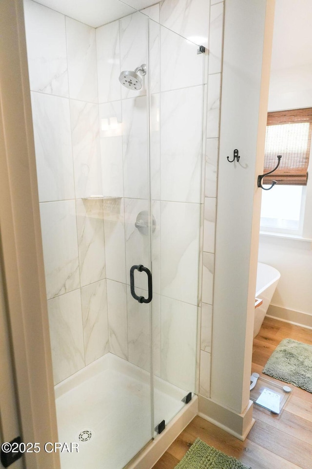 full bath with a soaking tub, a stall shower, baseboards, and wood finished floors