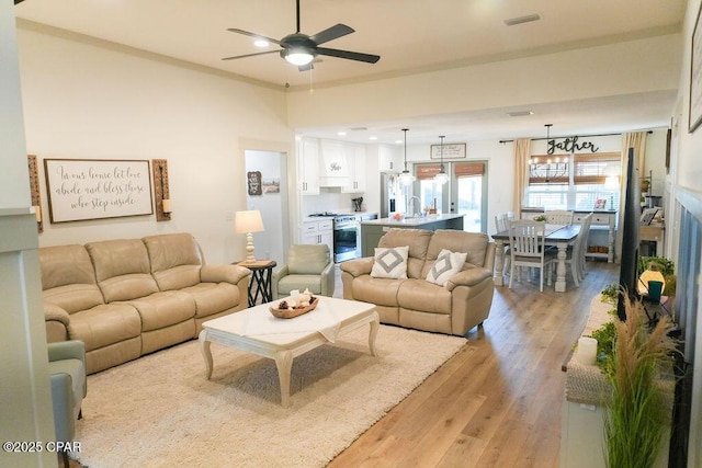 living room with visible vents, light wood-style floors, a fireplace, and a ceiling fan