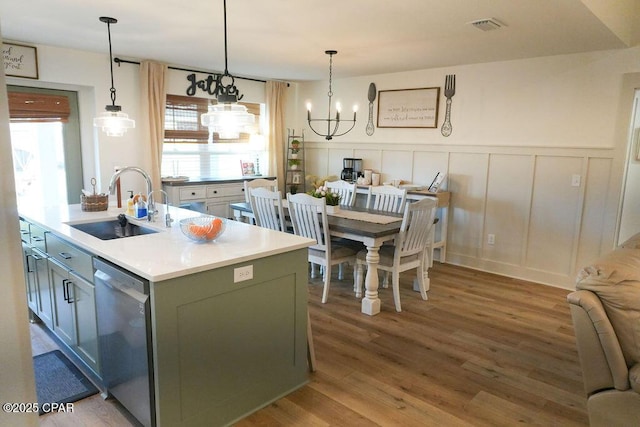 kitchen with light wood-type flooring, a kitchen island with sink, a sink, light countertops, and dishwasher