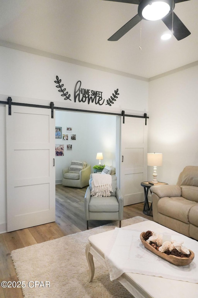 living area featuring ceiling fan, light wood-style floors, and a barn door