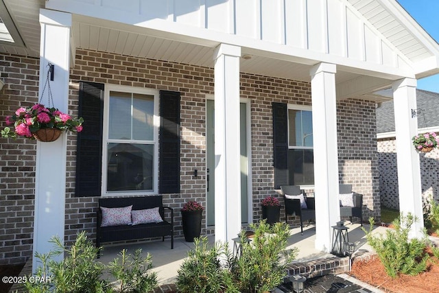 entrance to property featuring a porch, board and batten siding, and brick siding