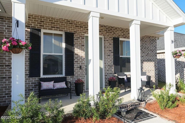 doorway to property featuring a porch, brick siding, and board and batten siding