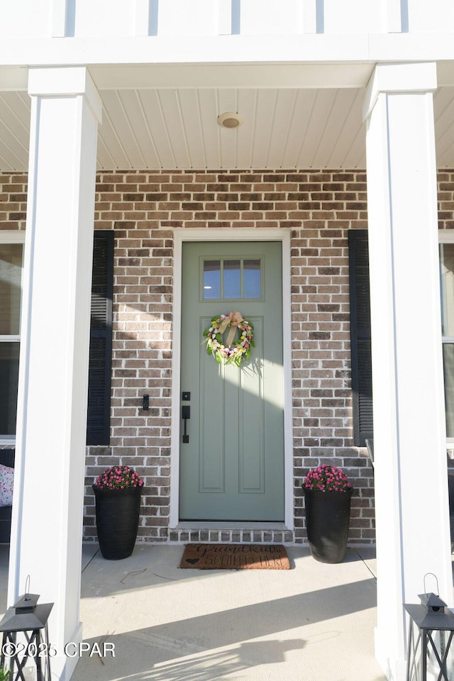 doorway to property with covered porch and brick siding