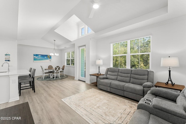 living room with ceiling fan with notable chandelier, baseboards, light wood-type flooring, and lofted ceiling