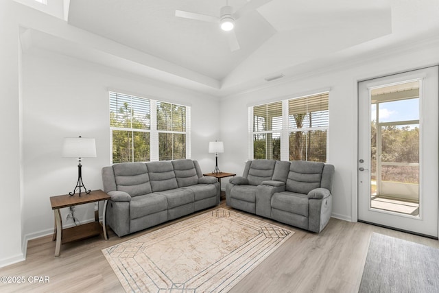 living room with baseboards, ceiling fan, a tray ceiling, lofted ceiling, and light wood-style flooring