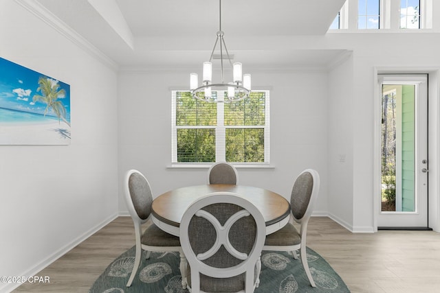 dining area featuring an inviting chandelier, baseboards, light wood-type flooring, and a raised ceiling