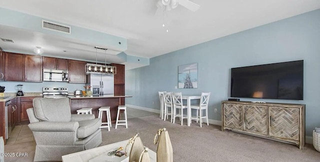 living room with ceiling fan with notable chandelier, light colored carpet, visible vents, and baseboards