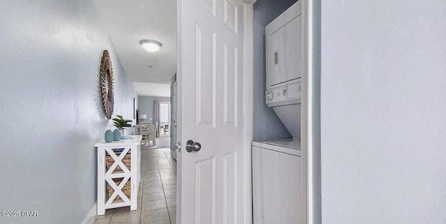 clothes washing area featuring stacked washer / dryer, light tile patterned floors, and baseboards