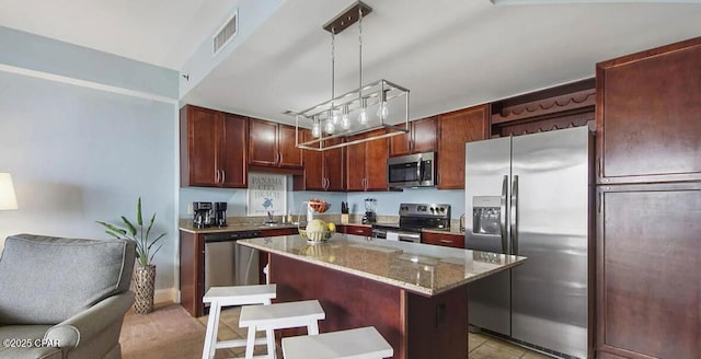 kitchen featuring visible vents, a center island, a kitchen bar, light stone counters, and appliances with stainless steel finishes