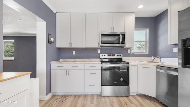 kitchen with light countertops, light wood-style floors, white cabinets, stainless steel appliances, and a sink