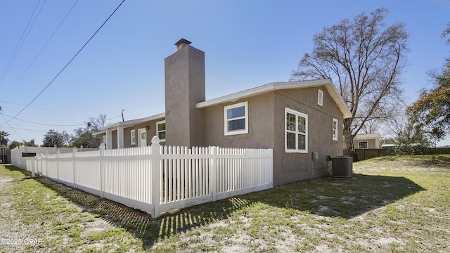 view of property exterior with cooling unit, a yard, a chimney, and fence