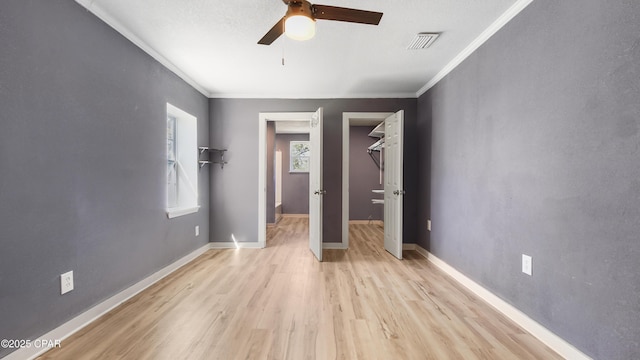 unfurnished bedroom featuring visible vents, a walk in closet, baseboards, crown molding, and light wood-style floors