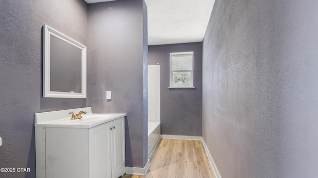 bathroom featuring baseboards, wood finished floors, vanity, and a textured wall