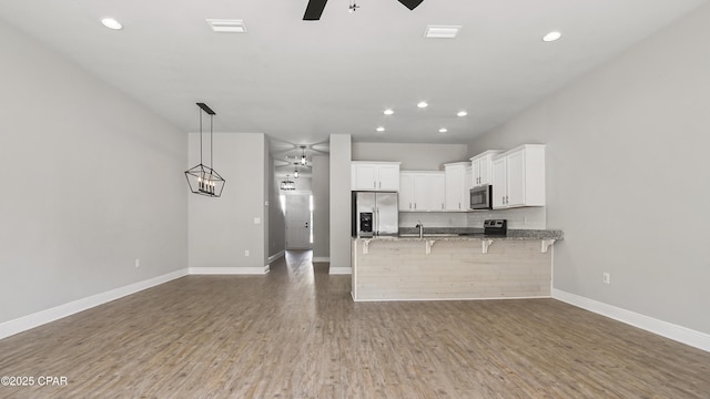 kitchen with wood finished floors, a peninsula, ceiling fan, stainless steel appliances, and white cabinets