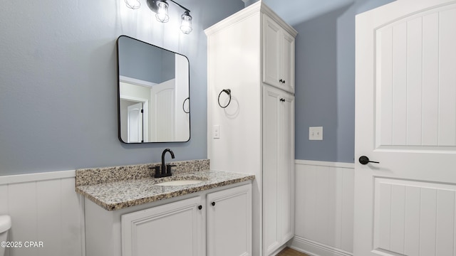 bathroom featuring a wainscoted wall, toilet, and vanity