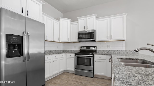 kitchen with light wood finished floors, a sink, appliances with stainless steel finishes, white cabinetry, and tasteful backsplash