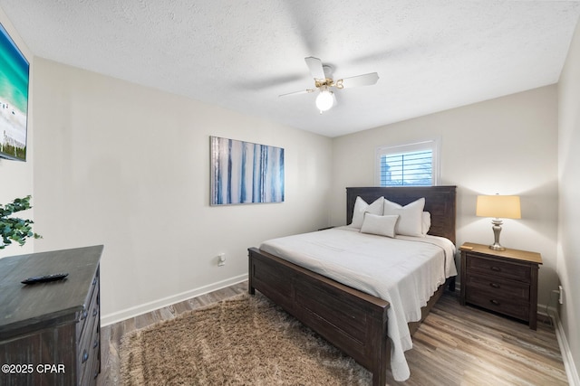 bedroom featuring ceiling fan, a textured ceiling, baseboards, and wood finished floors