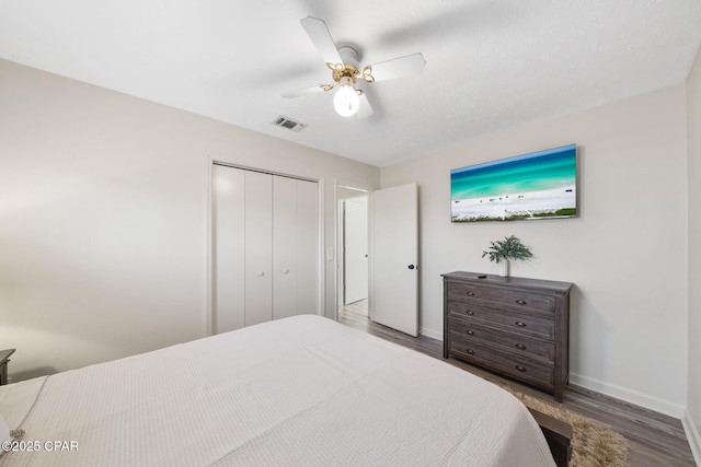 bedroom with visible vents, a ceiling fan, wood finished floors, a closet, and baseboards
