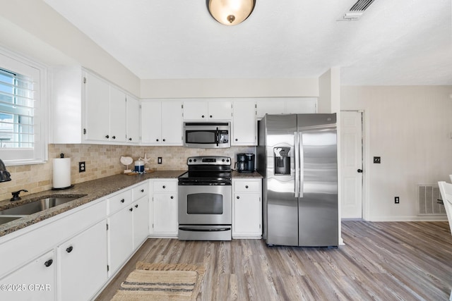 kitchen featuring a sink, stainless steel appliances, white cabinetry, light wood-type flooring, and backsplash