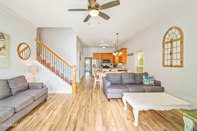 living room featuring baseboards, stairs, crown molding, ceiling fan with notable chandelier, and light wood-type flooring