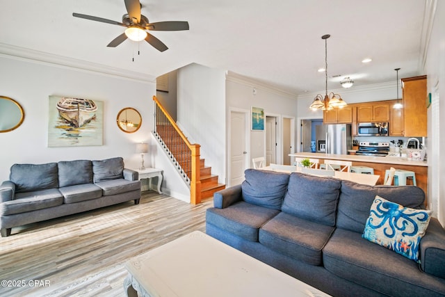 living area with ornamental molding, ceiling fan with notable chandelier, recessed lighting, light wood-style floors, and stairs