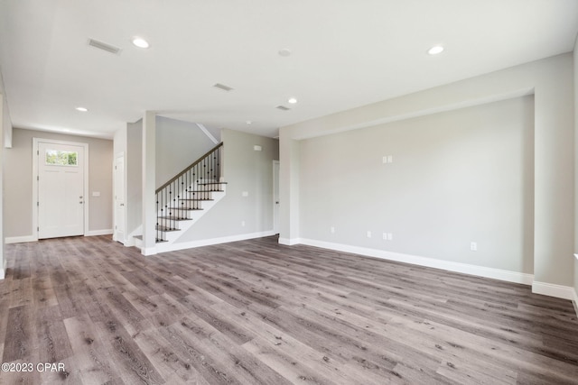 unfurnished living room with baseboards, stairs, visible vents, and wood finished floors